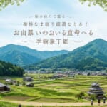 山々に囲まれた棚田と集落、五重塔のような建物がある日本の里山風景。
