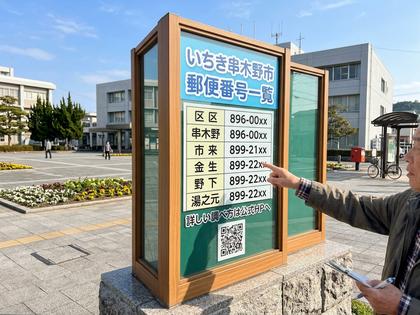 いちき串木野市の郵便番号一覧が書かれた掲示板を指さす男性。