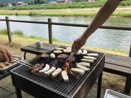 川沿いのバーベキュー場で食材を焼いている風景