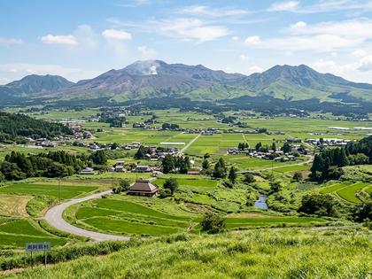噴煙を上げる阿蘇山と緑豊かな田園風景。
