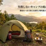 山と湖の夕焼けの絶景を背景に、テントとキャンプ道具が並ぶ風景。